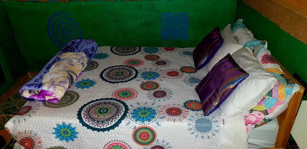 A bed with a patterned bedspread, pillows, and a rolled-up blanket.