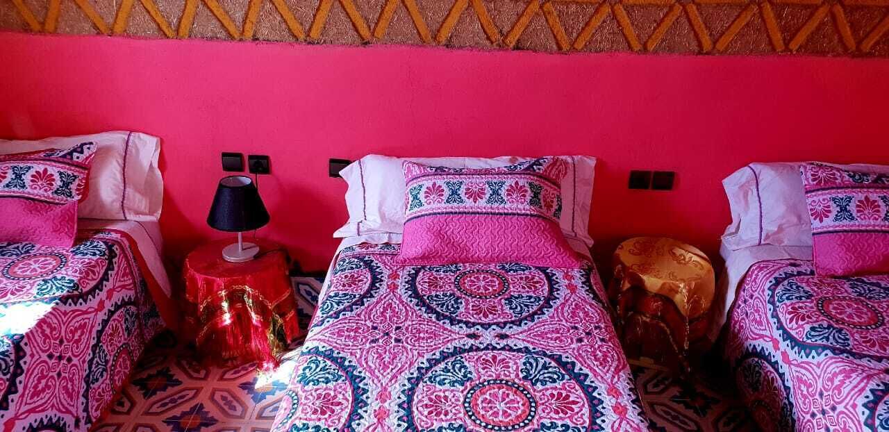 A room with three beds, each with patterned bedding and a red wall.