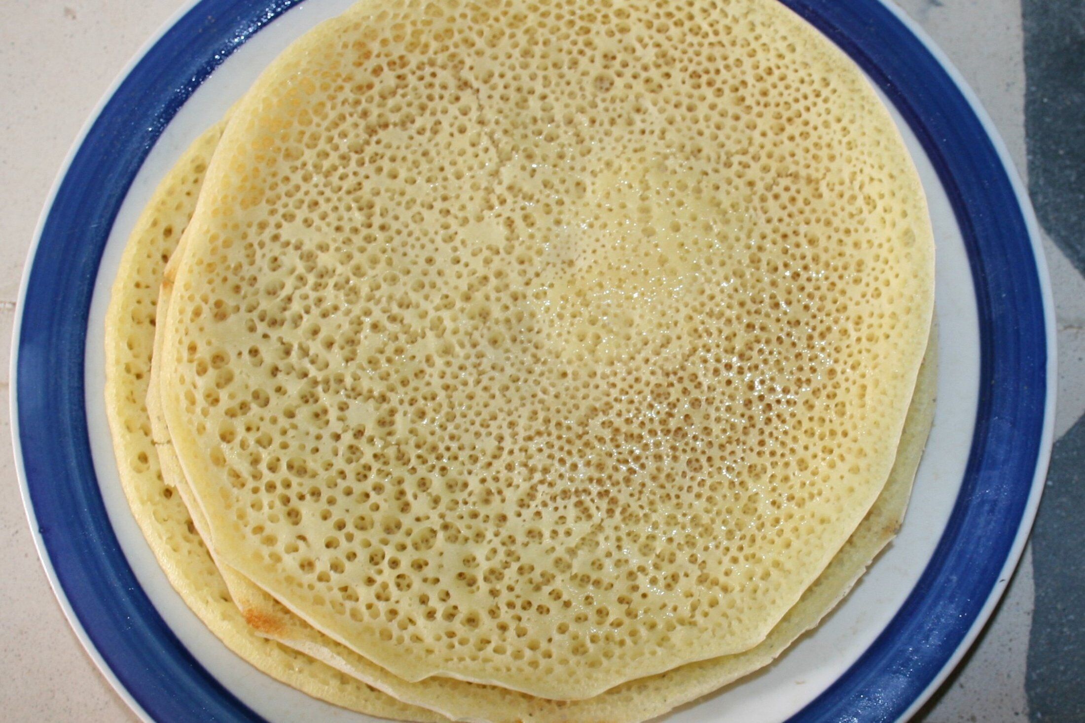 Una pila de crepes finos y redondos en un plato con borde azul.