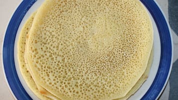 Una pila de crepes finos y redondos en un plato con borde azul.