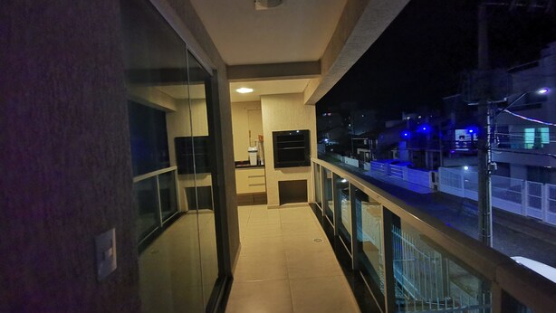 A narrow balcony with a glass railing overlooking a street at night. - Residencial Atalanta (Bombinhas)