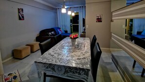 A dining area with a table covered in a patterned tablecloth, a sofa with cushions, and a mirror reflecting the room. - Residencial Atalanta (Bombinhas)