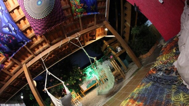 A wooden structure with a hammock, a hanging chair, and a bed with a patterned blanket. - Inefável Hostel Floripa (Florianópolis)