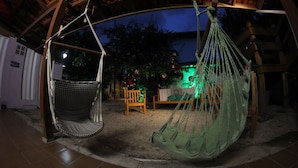 A hammock under a wooden structure, a wooden bench, and a small table with a cushion. - Inefável Hostel Floripa (Florianópolis)