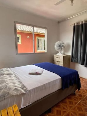 A bedroom with a bed, a window, a fan, and a curtain.