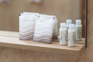 A bathroom shelf with toiletries including a towel, a shower gel, and several bottles of liquid soap.