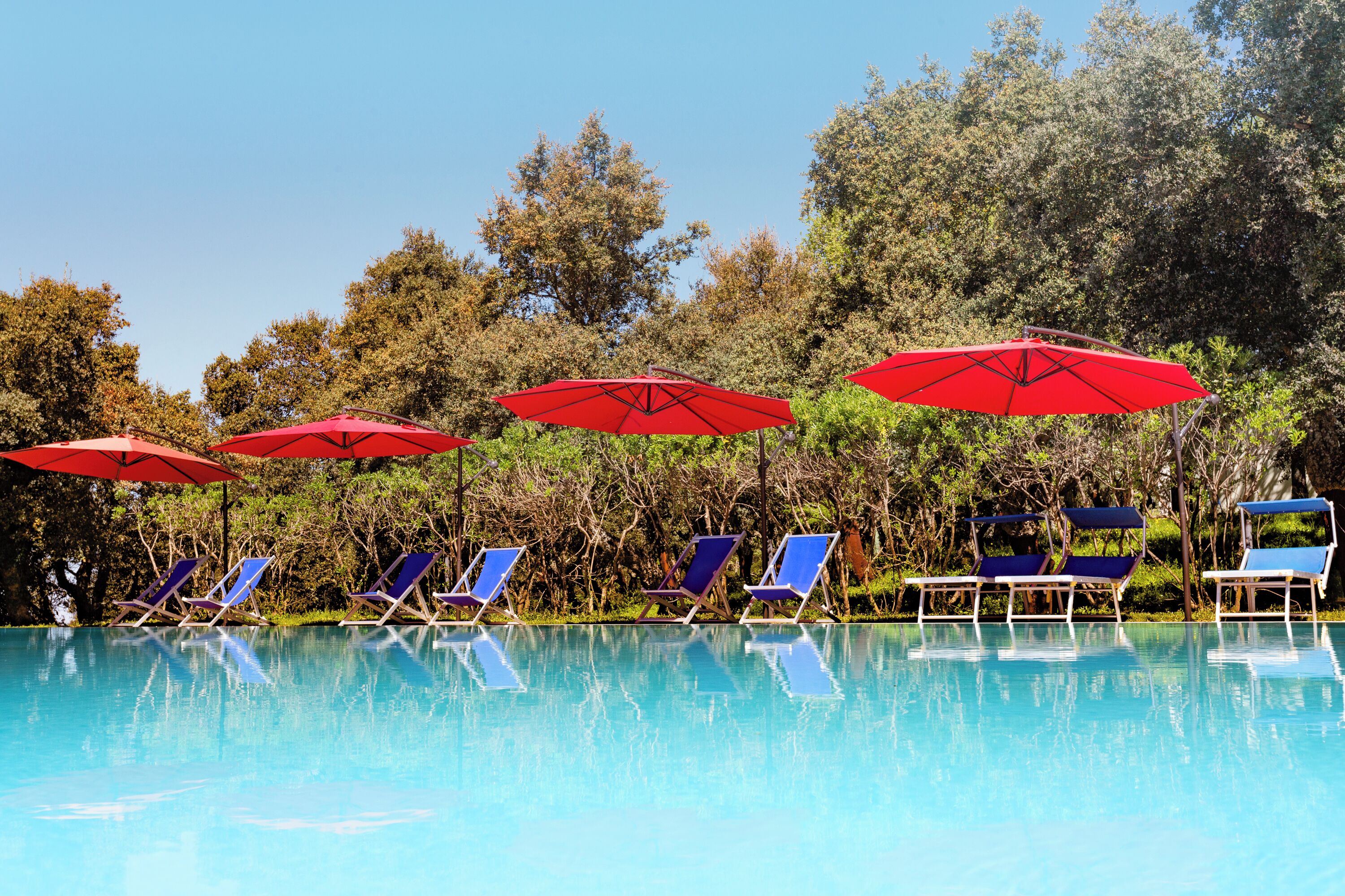 A pool area with blue lounge chairs and red umbrellas.
