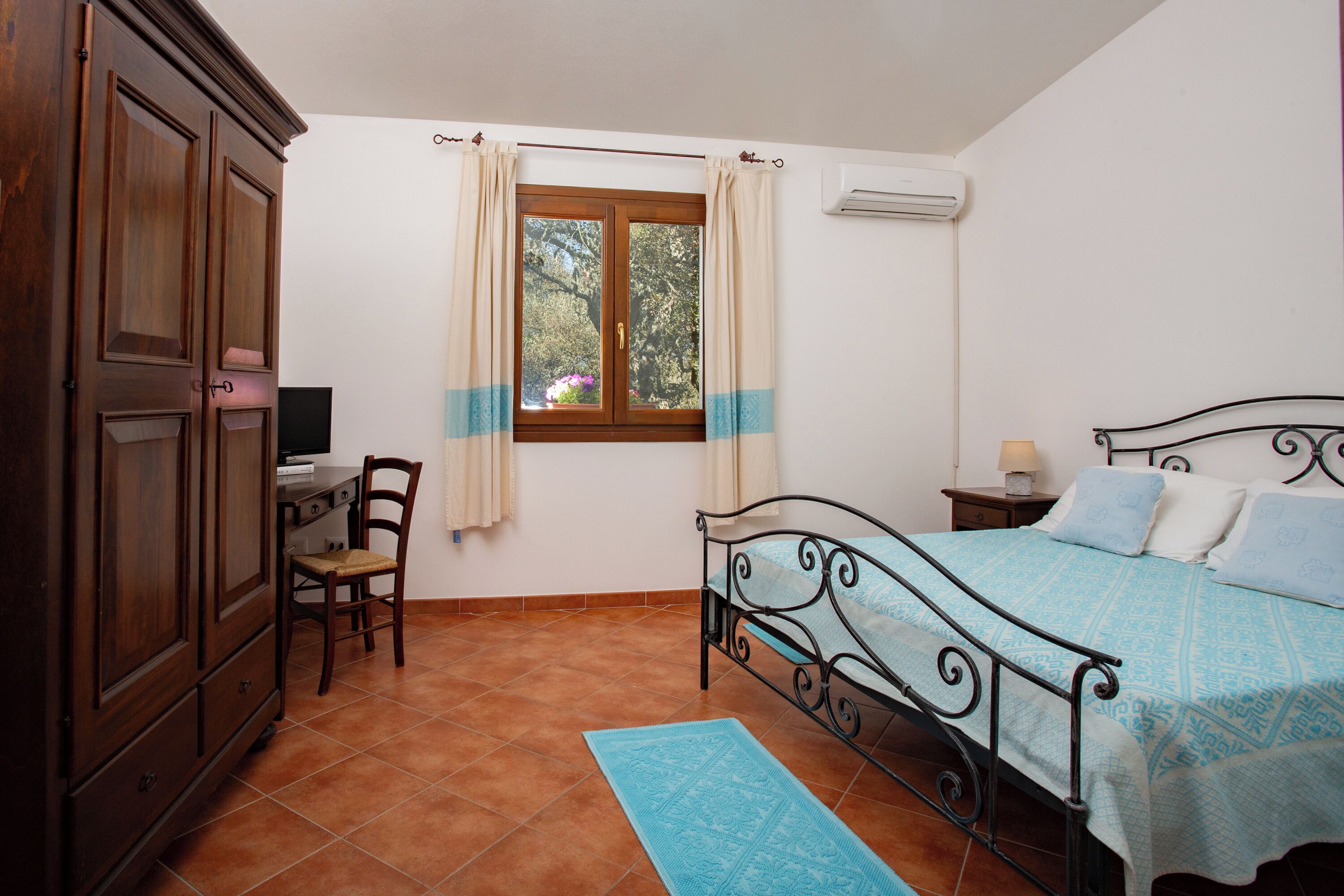 Un dormitorio con cama, escritorio, silla, armario y ventana con cortinas.