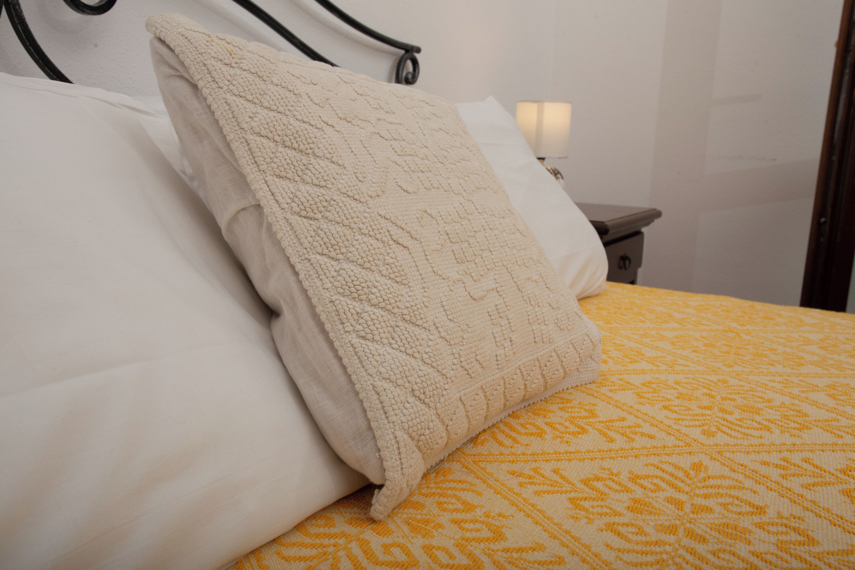 Ein Bett mit einer gelb gemusterten Tagesdecke und einem beige gestreiften Kopfkissen.