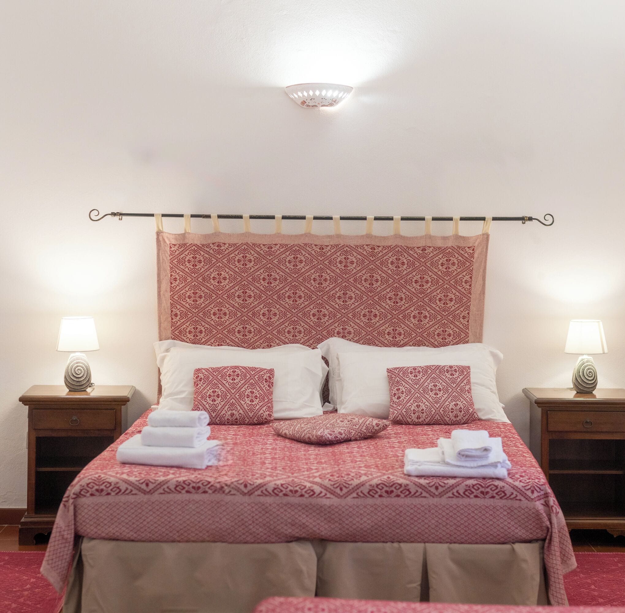 Una cama bien hecha con ropa de cama estampada, dos mesitas de noche con lámparas y un cabecero con un diseño decorativo.