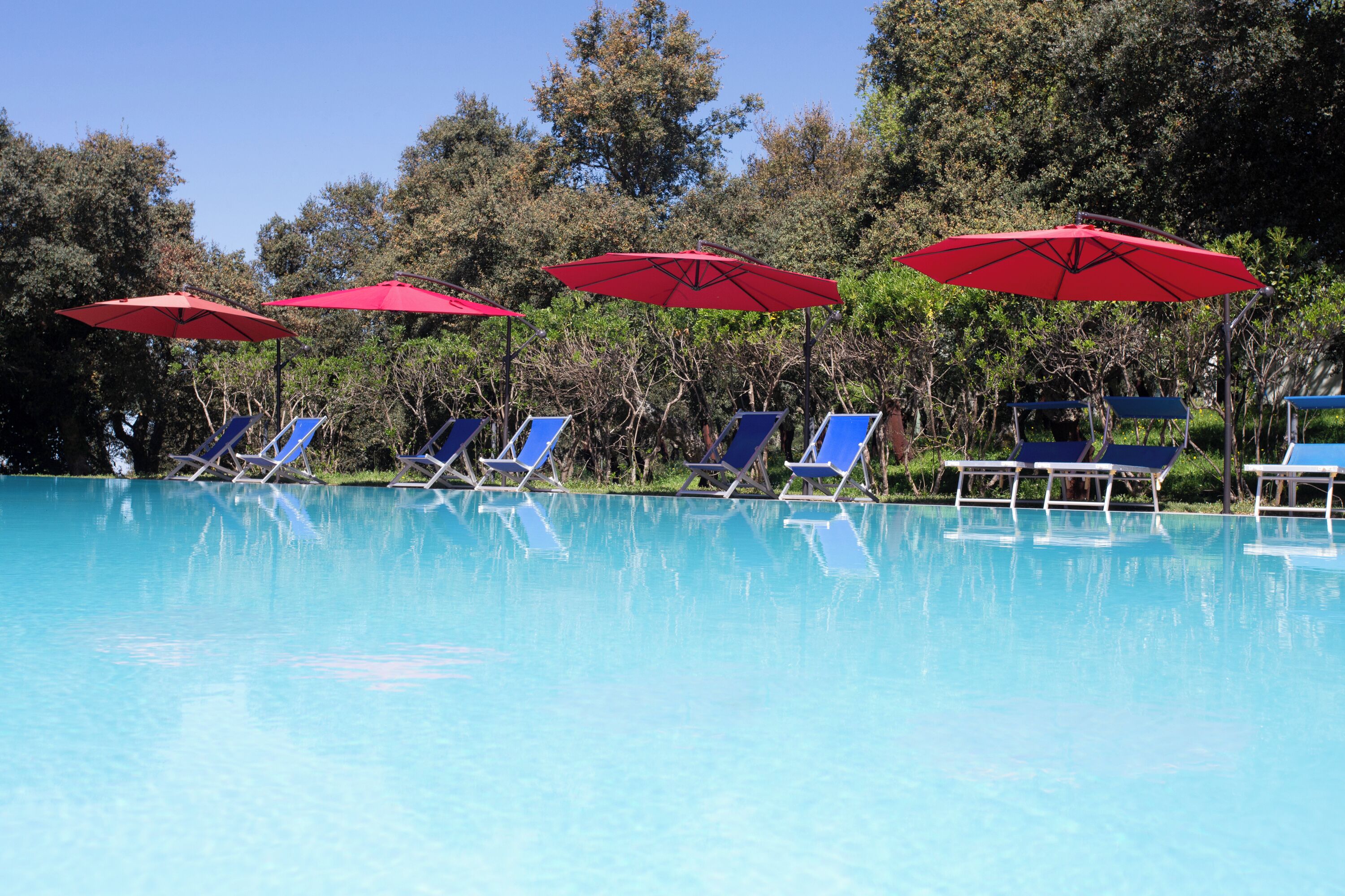 A clear blue pool with blue lounge chairs and red umbrellas.