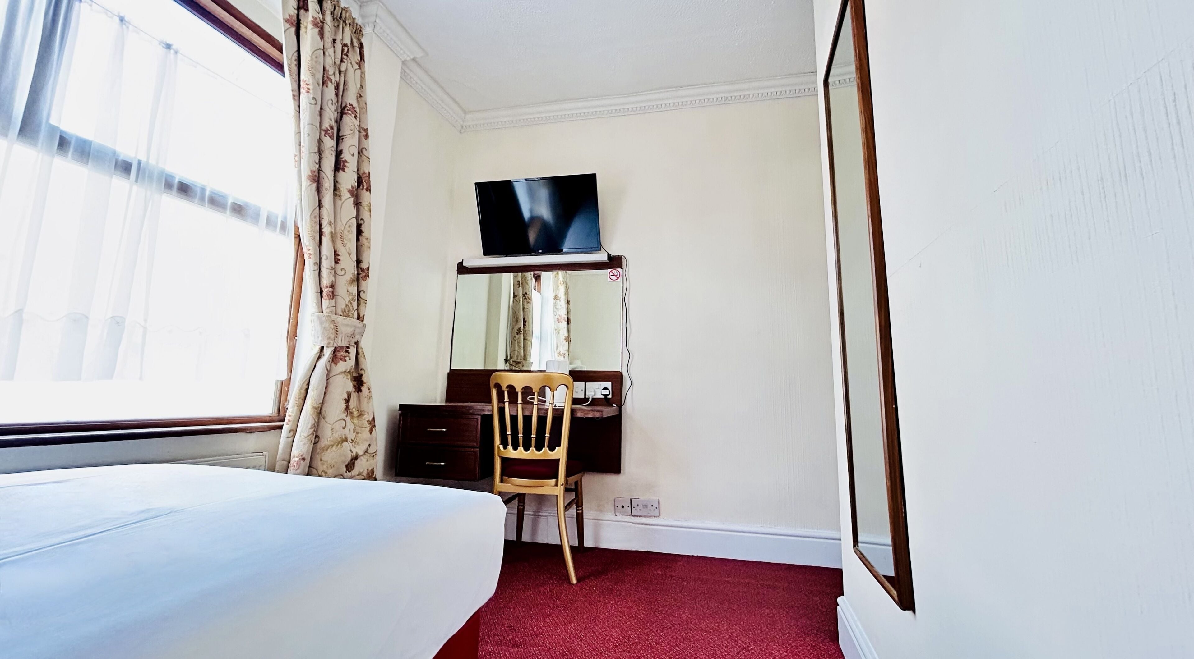 A hotel room with a bed, a desk with a chair, a television, and a large mirror.