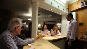 A group of people sitting at a wooden bar in a kitchen with a brick wall and wooden cabinets. - Columbia Hotel & Restaurant (Wellingborough)