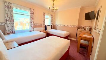 A hotel room with two beds, a wooden desk, a television, and a window with curtains.