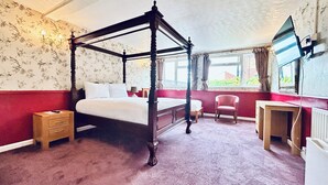 A four-poster bed with a wooden frame, a desk with a chair, and a radiator. - Columbia Hotel & Restaurant (Wellingborough)