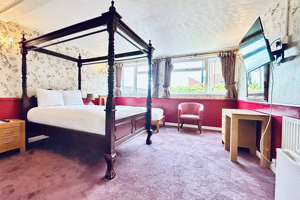 A four-poster bed with a wooden frame, a desk with a chair, and a radiator.