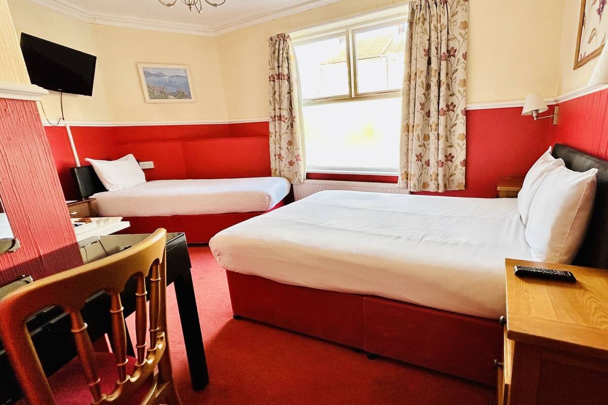 A hotel room with two beds, a desk, a chair, a TV, and a window with curtains.
