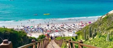 A wooden staircase leading to a beach with umbrellas and people.