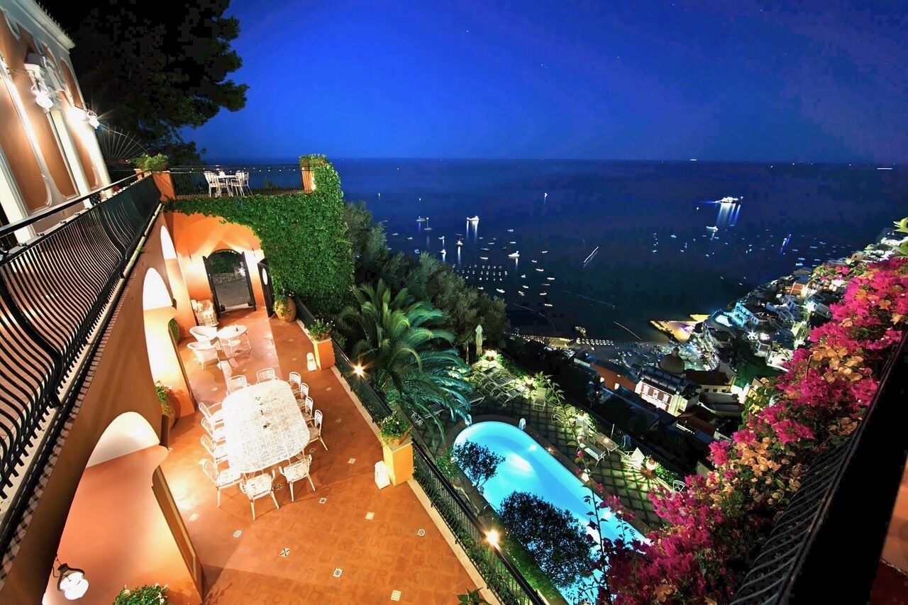 A rooftop terrace with a pool, outdoor seating, and a view of the cityscape at night.