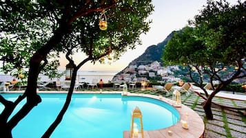 A poolside area with a view of a coastal town, surrounded by trees and outdoor seating.
