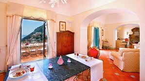 Un coin repas avec une table dressée pour deux personnes, une vue sur un paysage montagneux par de grandes fenêtres et un lustre.