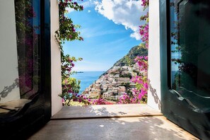 Uitzicht vanuit een raam op een kustplaatsje met gebouwen op een heuvel en bougainvillea bloemen.