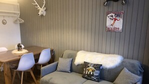 Un espacio habitable acogedor con un sofá gris, una mesa de comedor de madera con sillas, una cabeza de ciervo decorativa y un póster en la pared.