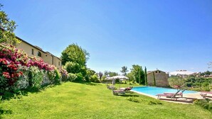 Un jardin avec une piscine, des chaises longues et une pelouse verdoyante.