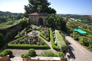 A landscaped garden with a central fountain, a pool, and a small building with a tiled roof.