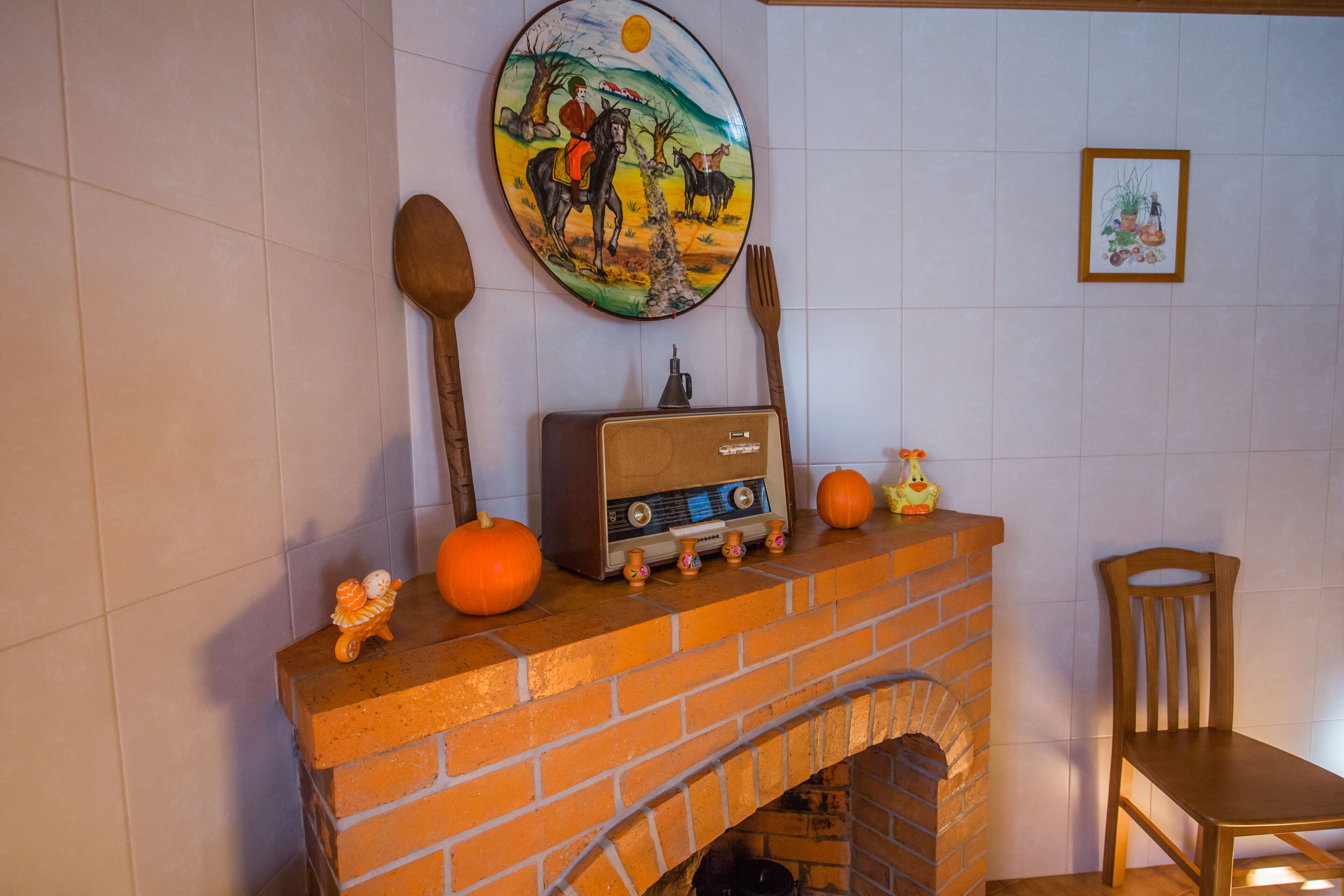A fireplace with a radio, wooden utensils, and pumpkins on top.