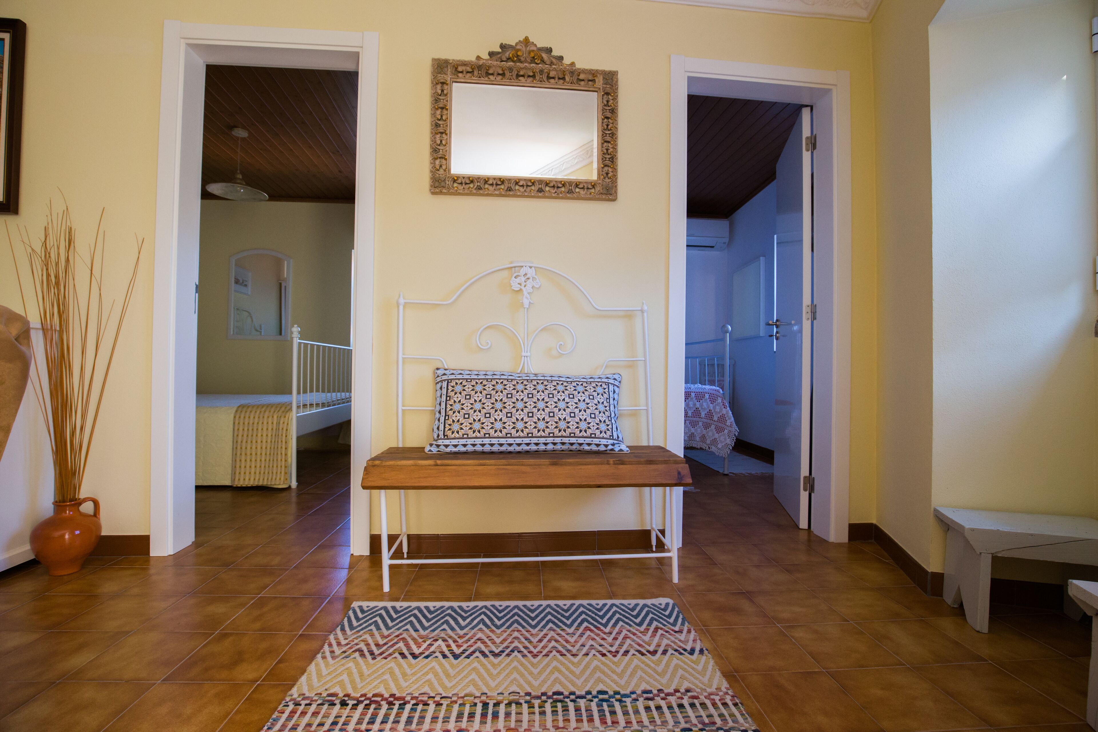 A hallway with a bench, a patterned rug, and a mirror on the wall.