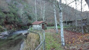 A stone building with a red roof near a river, surrounded by trees and a stone wall. - Cabanelas Country House Casa do Afonso (Vale de Cambra)