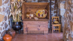 A rustic stone wall with a wooden chest containing corn cobs, a basket, and a small house model. - Cabanelas Country House Casa do Afonso (Vale de Cambra)