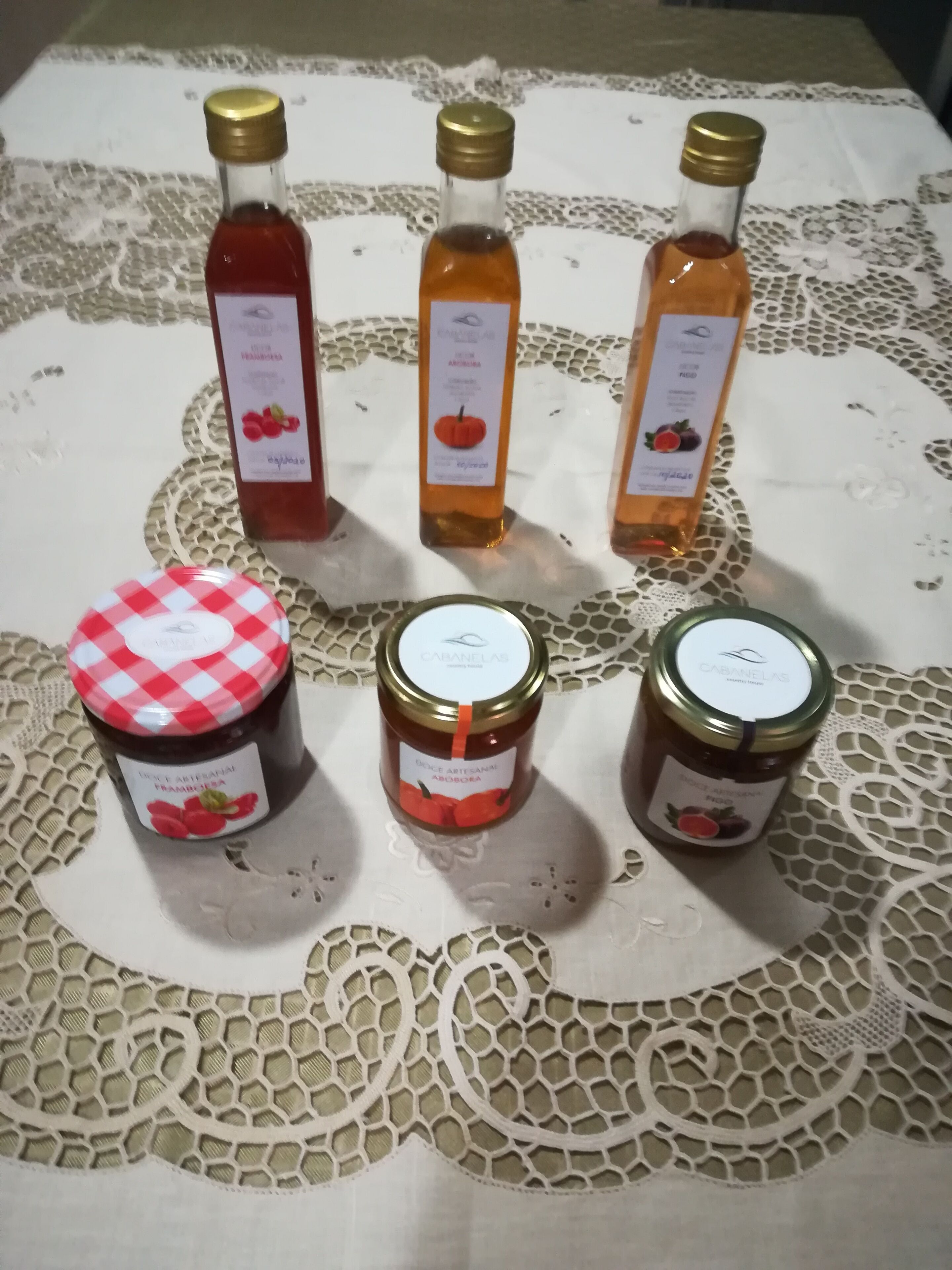 Une table sur laquelle sont disposés cinq pots de confiture et deux pots de miel, tous étiquetés, sur une nappe en dentelle.