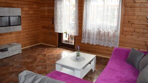 A wooden cabin interior with a purple sofa, white coffee table, and lace curtains.
