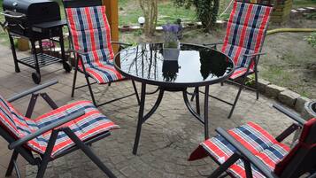 A patio with four striped chairs, a round table, and a grill.