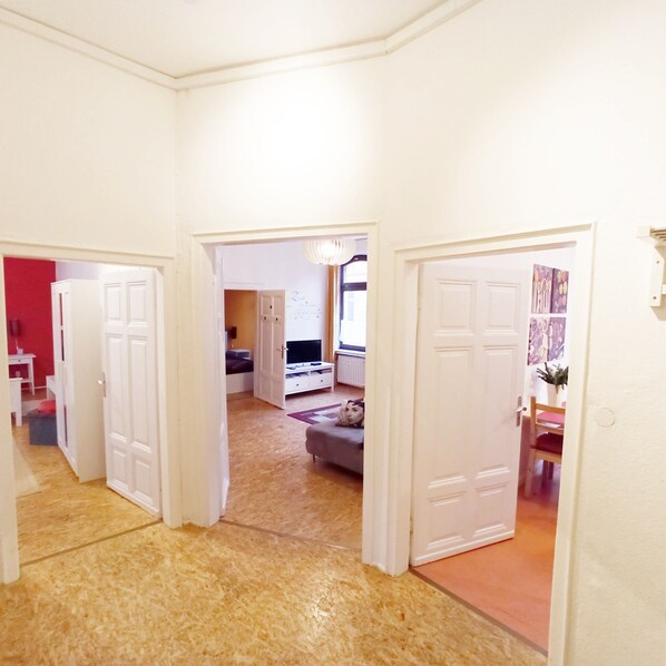 A hallway with white doors leading to a living area with a sofa and a television.