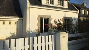 Une maison à deux étages avec une façade blanche, un toit noir et une clôture blanche faite de piquets.