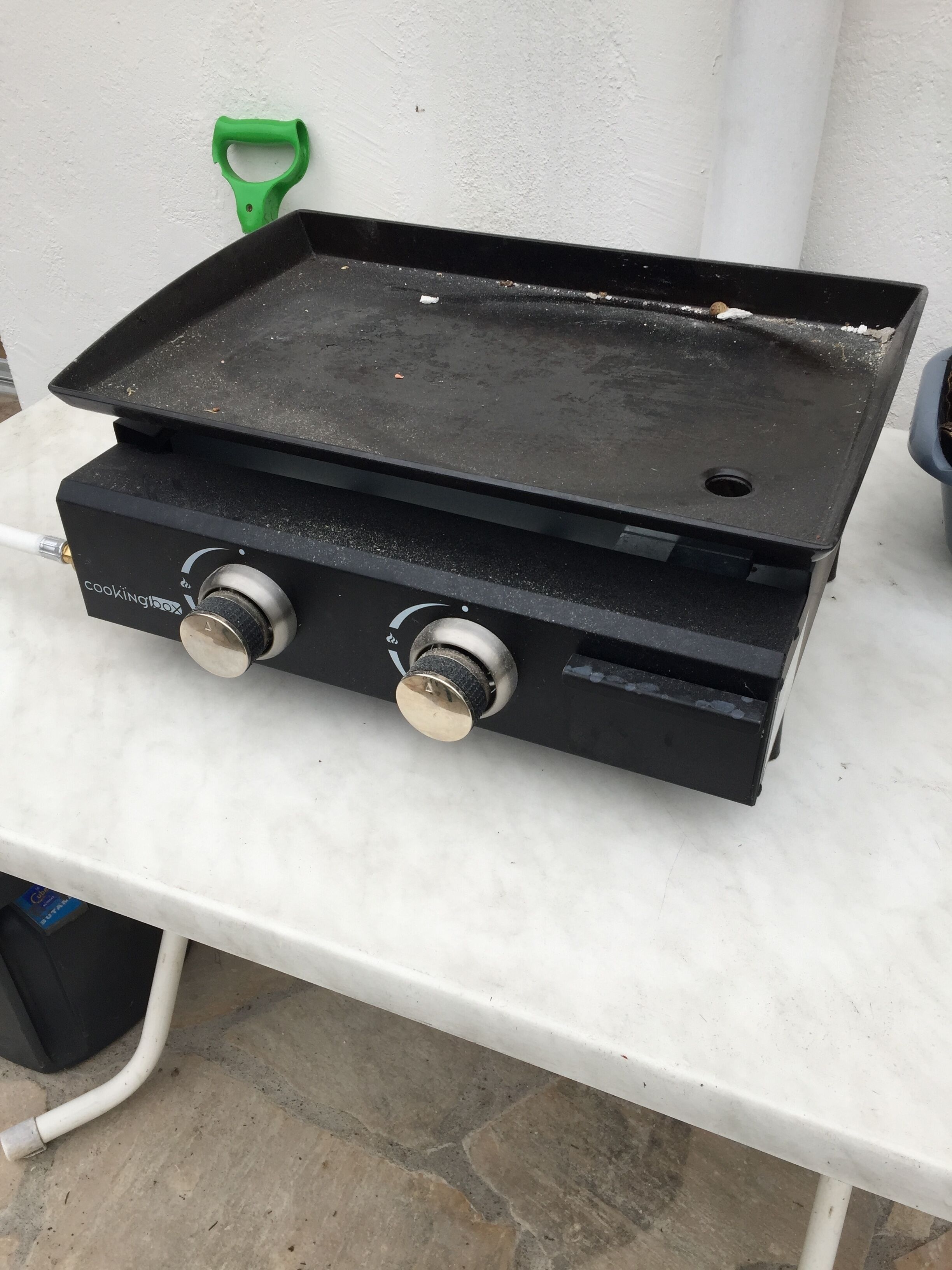 A portable cooking stove with two knobs and a flat cooking surface, placed on a white table.