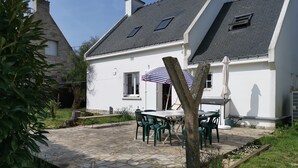 Une maison blanche avec un patio en pierre, un espace salon extérieur et un arbre au premier plan.