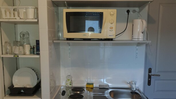 A compact kitchen with a microwave, kettle, and coffee maker on the countertop. There is a sink with a dish rack, and a trash bin is visible. - Residence Terminus housing  (Clermont-Ferrand)
