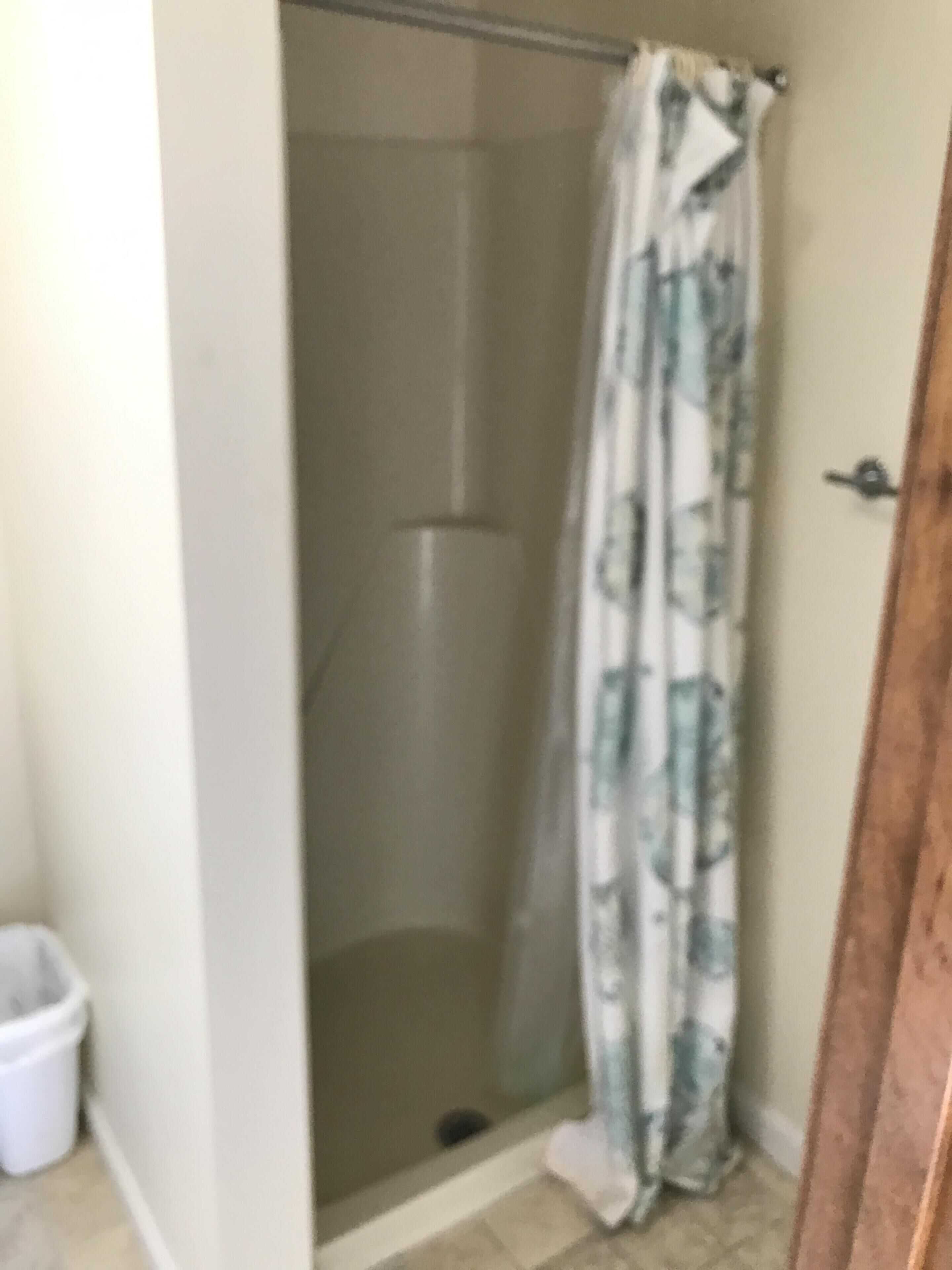 Un baño con ducha, inodoro y un cubo blanco.