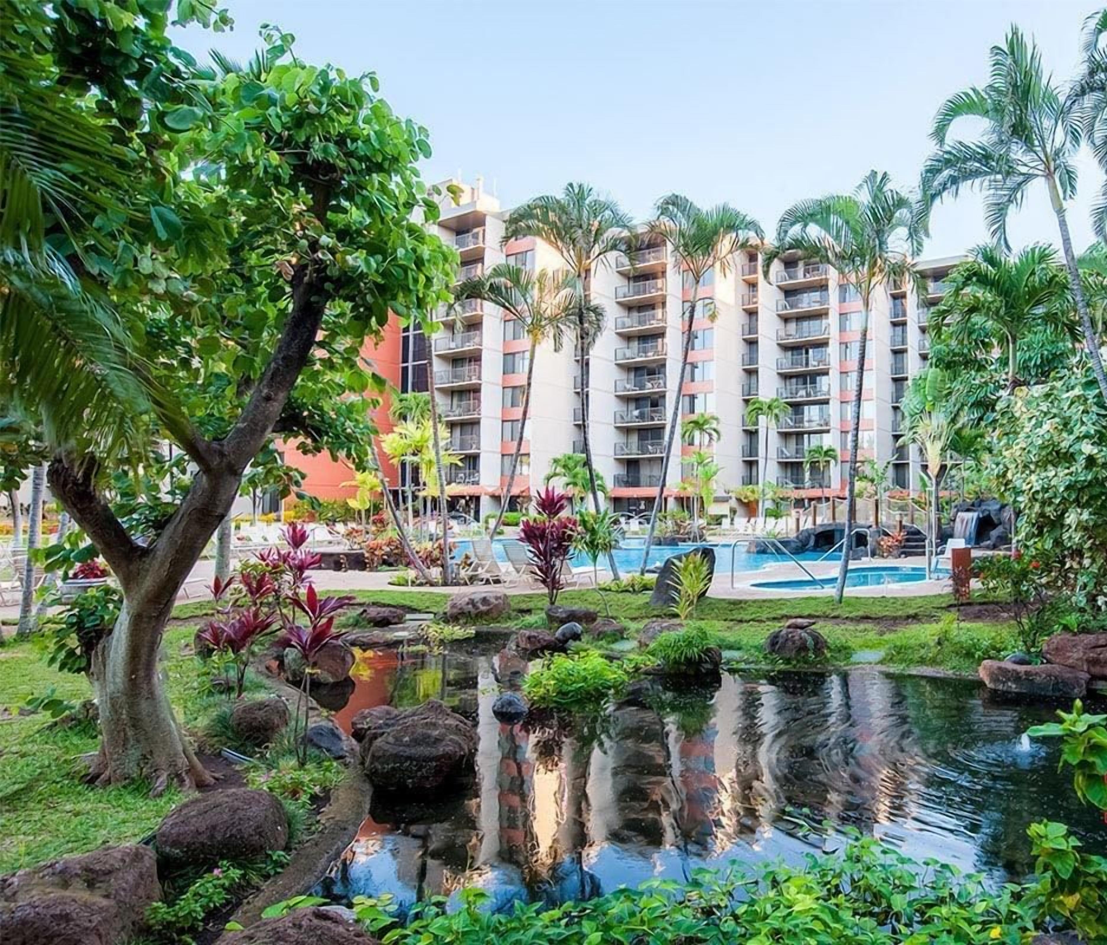A hotel with a pool, lush greenery, and a pond.