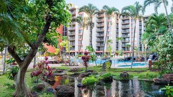 A hotel with a pool, lush greenery, and a pond.