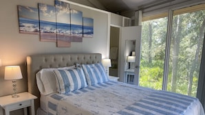 Camera da letto con un letto grande, due comodini con lampade, una finestra vista alberi e tre quadri appesi al muro.