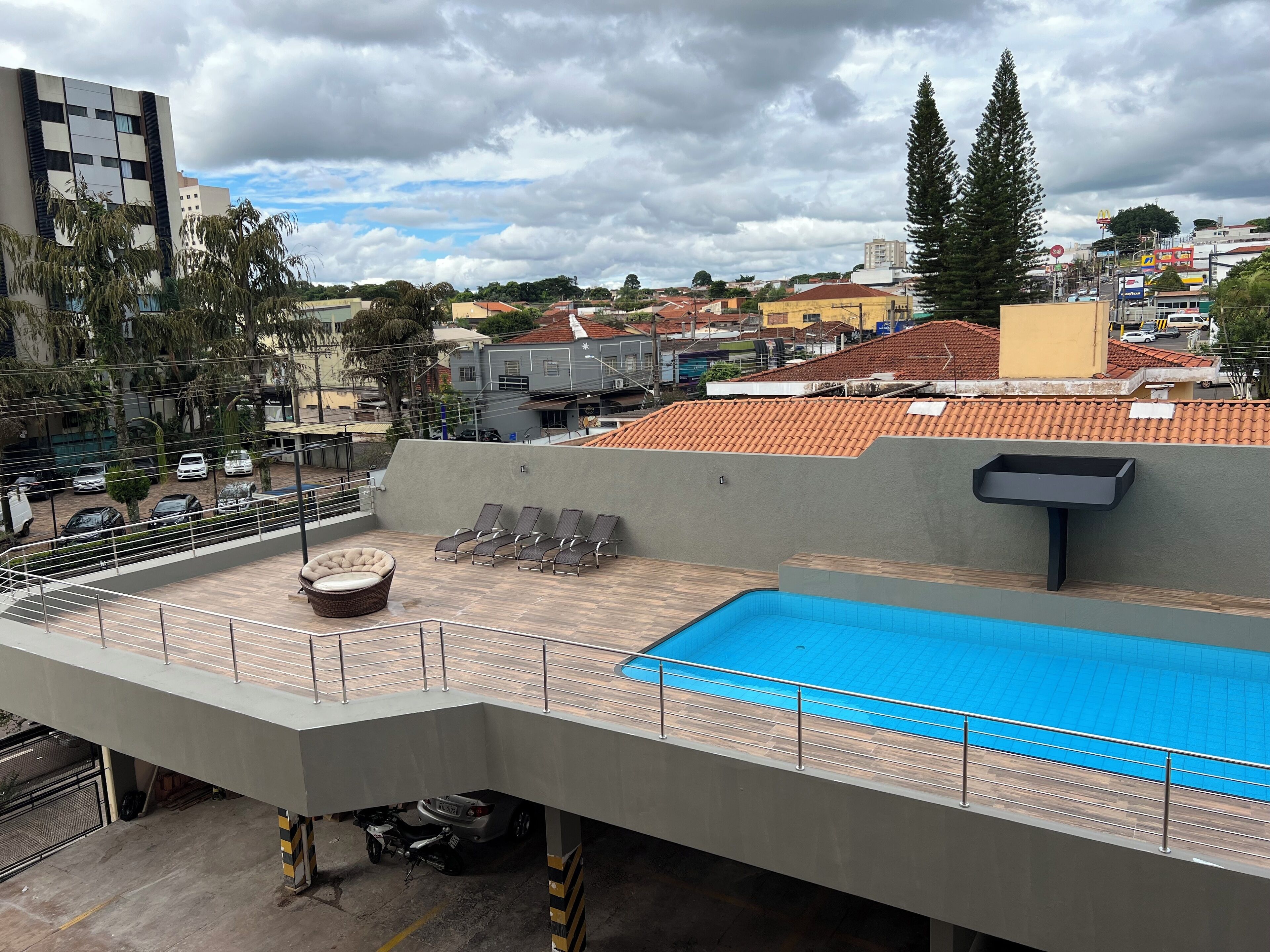 A rooftop pool area with lounge chairs, a small seating area, and a view of the surrounding cityscape.