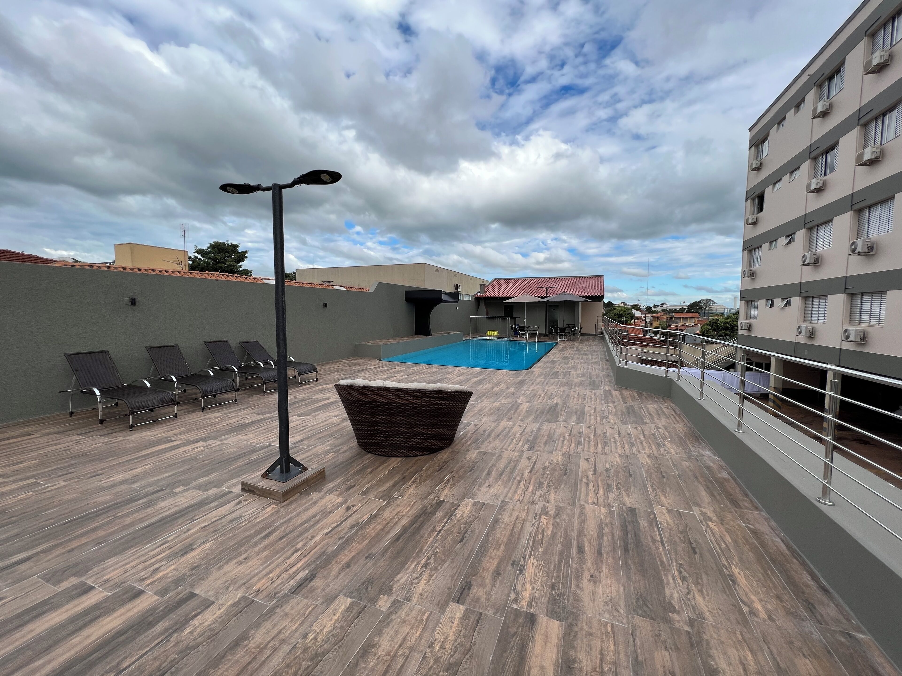 Un área de piscina en la azotea con sillones de descanso, una silla de mimbre y una mesa.