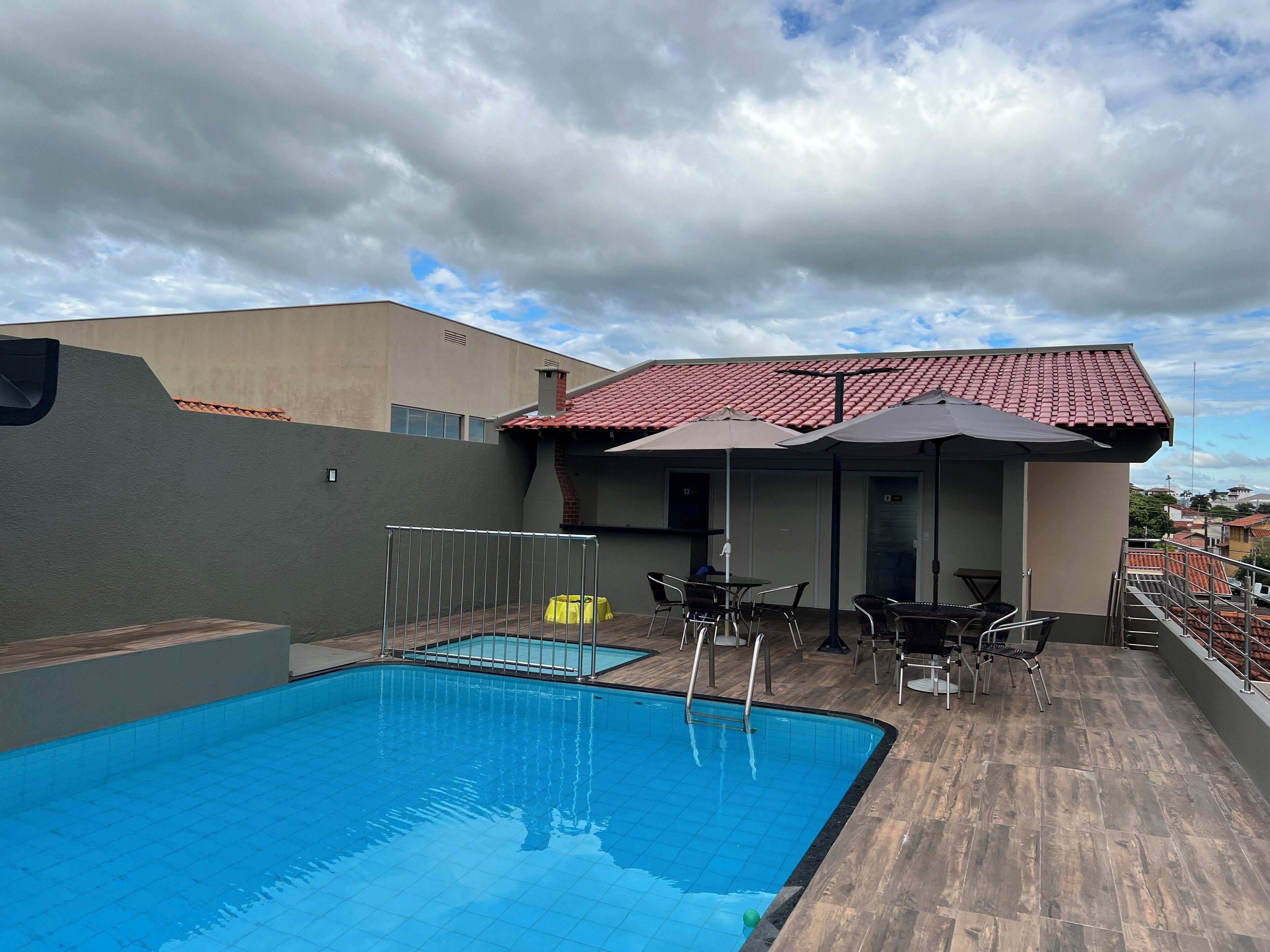 A rooftop swimming pool with a tiled deck, outdoor seating, and a covered patio area.
