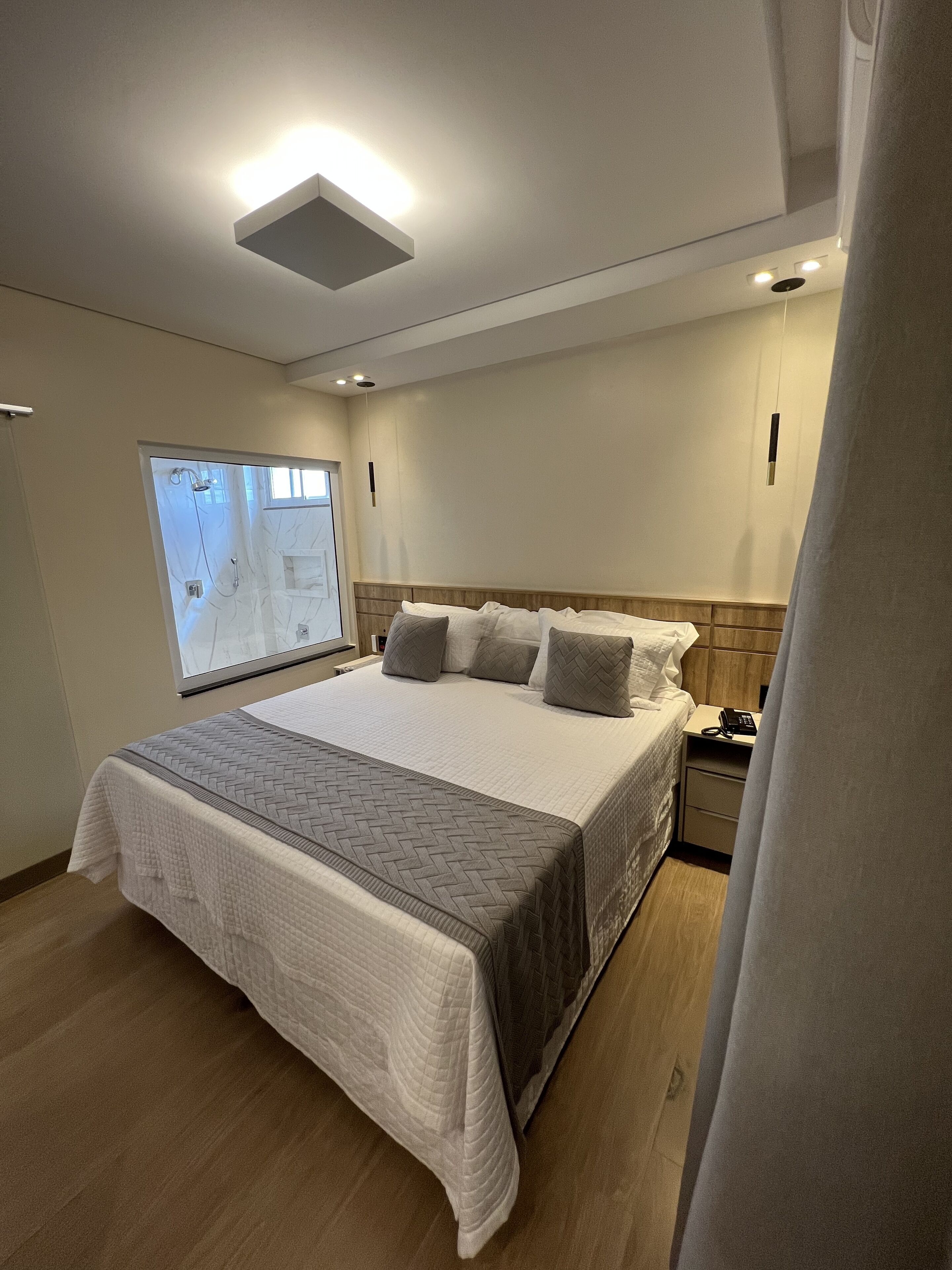 A modern hotel room with a large bed, a bedside table with a phone, and a shower area visible through a glass door.