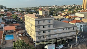 Un hôtel à plusieurs étages, doté d’un toit plat, de climatiseurs et d’un parking où sont stationnés plusieurs véhicules.